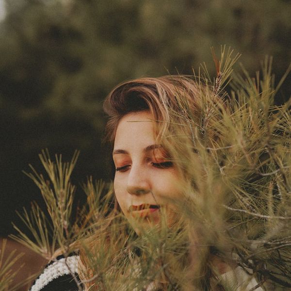 Woman meditating outdoors surrounded by green nature.